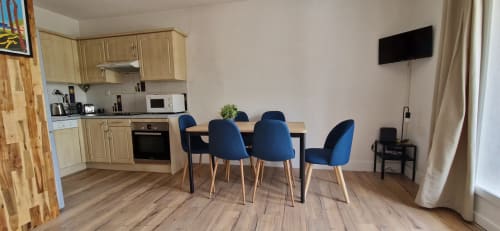 Élégante salle à manger avec chaises bleues, cuisine et téléviseur dans l'appartement O SOLEIL à Saint-Cyr-sur-Mer