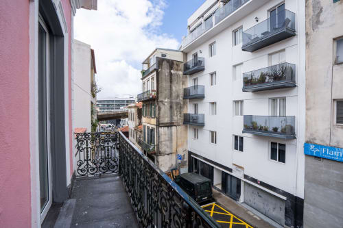 Vista da varanda do hotel Madeirarooms em Funchal com rua da cidade, edifícios brancos e grade de ferro ornamentada