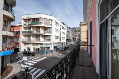 Vista da varanda de rua em Funchal com edifícios coloridos e montanhas, hotel Madeirarooms