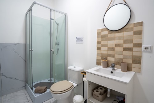 Banheiro moderno do Madeirarooms Funchal com chuveiro em vidro, pia branca, azulejo bege e espelho redondo