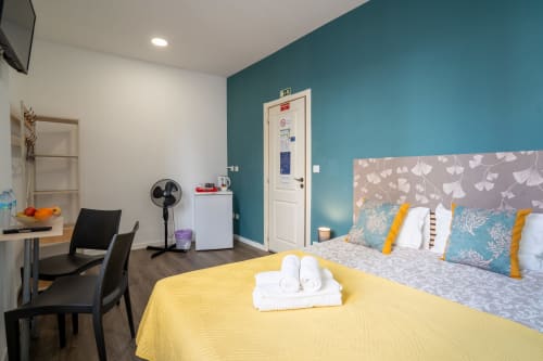 Quarto duplo moderno do Madeirarooms em Funchal com parede de destaque azul-petróleo, roupa de cama amarela e vista para a cidade