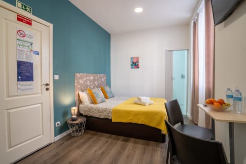 Quarto duplo luminoso na Madeirarooms Funchal com roupa de cama amarela, paredes azul-petróleo e comodidades modernas