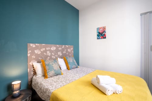 Quarto duplo moderno na Madeirarooms Funchal com parede de destaque azul-turquesa, cabeceira floral e roupa de cama amarela