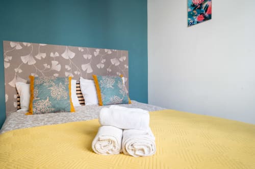 Quarto duplo Madeirarooms em Funchal com roupa de cama amarela, cabeceira estampada e toalhas enroladas