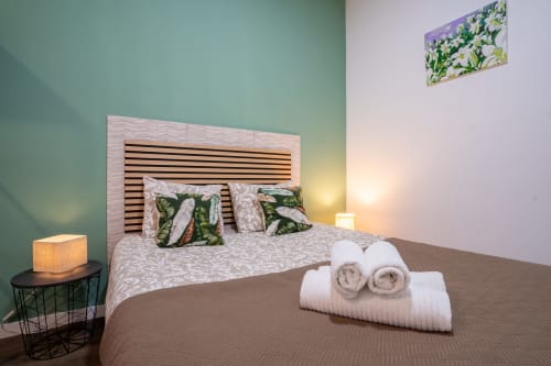 Quarto de casal moderno no hotel Madeirarooms em Funchal com cabeceira listrada, toalhas enroladas e paredes com destaque verde