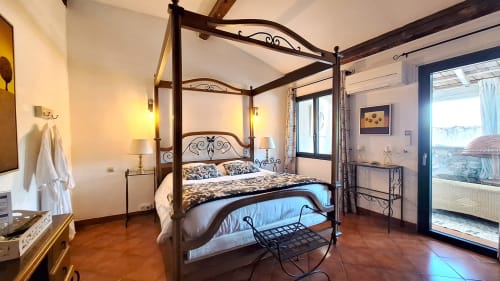 Suite lune de miel élégante à La Bergerie Du Moulin avec lit à baldaquin en fer forgé, sols en terre cuite et balcon vue piscine
