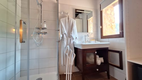 Salle de bain moderne à La Bergerie Du Moulin avec douche, vasque blanche, miroirs, meuble sombre et peignoirs à Taradeau
