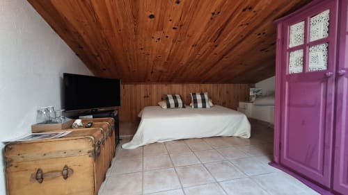 Chambre mansardée à La Bergerie Du Moulin : plafond bois, lit blanc, TV, malle vintage et armoire rose à Taradeau
