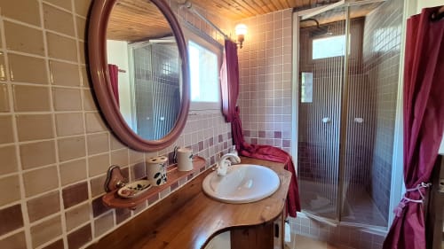 Salle de bain spacieuse à La Bergerie Du Moulin avec lavabo en bois, miroir rond, douche et touches de couleur bordeaux
