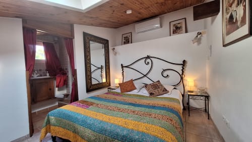 Chambre de La Bergerie Du Moulin avec lit en fer forgé, linge rayé coloré, plafond en bois et salle d'eau attenante