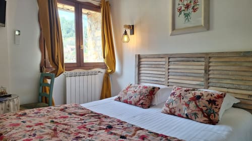 Chambre cosy à La Bergerie Du Moulin avec parure florale, tête de lit en bois et rideaux dorés à Taradeau