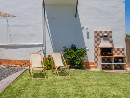 Dos tumbonas color crema en jardín verde con chimenea de ladrillo rojo y villa blanca en Alhaurín Loft City Center, España