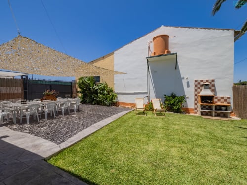 Villa loft Alhaurín con patio de césped verde, edificio blanco, depósito de agua terracota, tumbonas de madera y horno tradicional