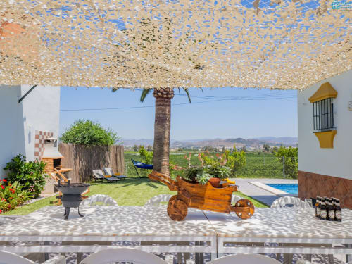 Terraza de villa con palmera, macetero de carreta de madera, tumbonas, vista a la piscina y paisaje rural en Alhaurín de la