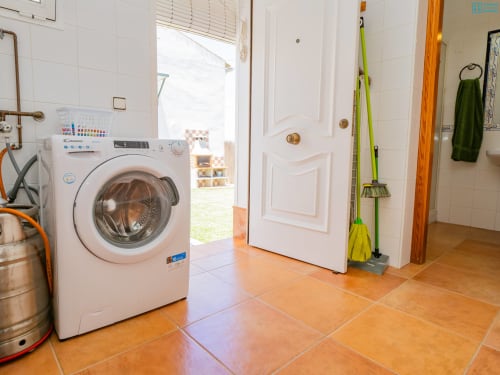 Lavadero con lavadora blanca, piso de baldosas terracota y productos de limpieza en la villa Riad de Maruchi