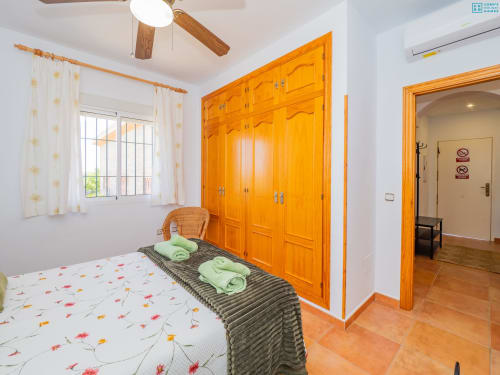 Dormitorio luminoso en Alhaurín Loft con ropa de cama floral colorida, amplio armario de madera naranja, ventana con cortinas blancas