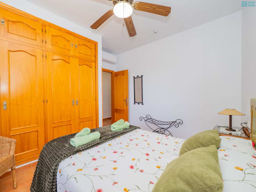 Dormitorio luminoso en la villa Alhaurín Loft con armario de madera, ropa de cama floral, almohadas verdes, ventilador de techo y paredes blancas
