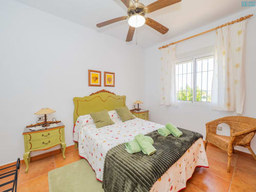 Dormitorio luminoso en Alhaurín Loft con cabecero amarillo, almohadas verdes y suelos de terracota con silla de mimbre