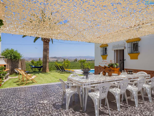 Patio exterior de la villa Riad de Maruchi en Alhaurín de la Torre con mesa de comedor, palmera, toldo, piscina y montaña
