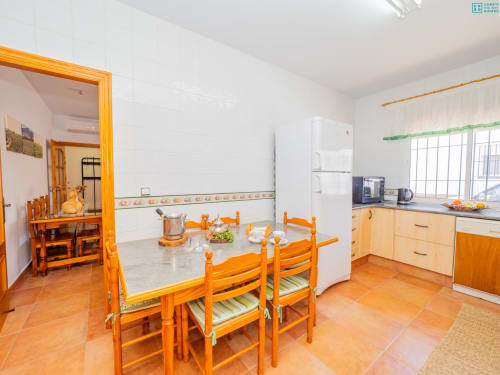 Cocina-comedor luminoso con mesa de madera, sillas, electrodomésticos blancos y suelo de baldosas naranjas en la villa Riad de Maruchi