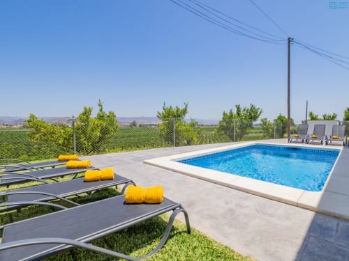 Área de descanso junto a la piscina de la villa Alhaurín Loft con piscina rectangular azul, toallas amarillas enrolladas en tumbonas oscuras y montañas