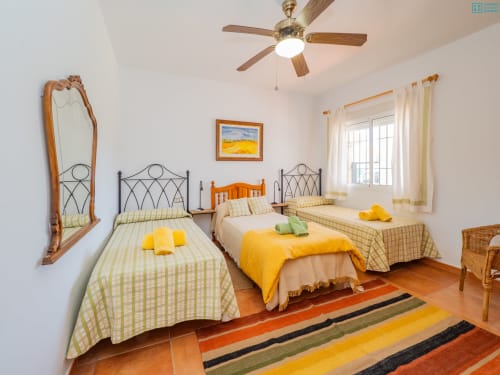 Dormitorio amplio y luminoso en Alhaurín Loft con tres camas, vigas de madera, alfombra de rayas y detalles amarillos
