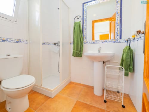 Baño moderno con suelo de azulejos naranja, lavabo blanco, ducha cerrada y toallas verdes en villa Alhaurín Loft City Center