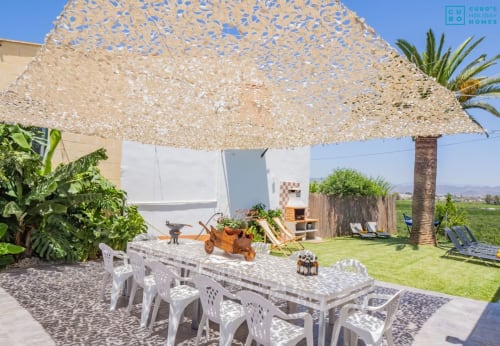 Terraza exterior de la villa Riad de Maruchi con mesa de comedor, sombra natural, palmeras y vistas a las montañas en Alhaurín de la