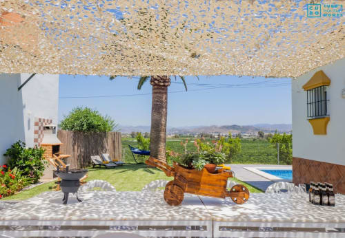 Terraza de villa Riad de Maruchi con vistas a la piscina, palmera, macetero de carrito de madera y vistas del valle de Alhaurín