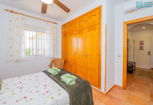 Dormitorio luminoso en Alhaurín Loft con armarios de madera naranja, cama doble y toallas verdes en banco