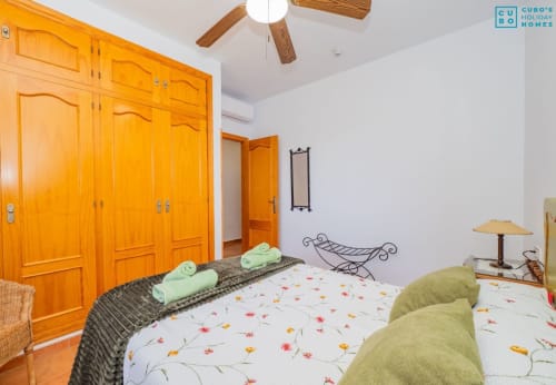 Dormitorio luminoso en la villa Riad de Maruchi con armario de madera, ropa de cama floral y sillones verdes en Alhaurín de la Torre.