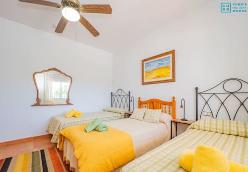 Dormitorio luminoso de la villa Alhaurín Loft con tres camas, acentos amarillos, ventilador de techo de madera y alfombra rayada colorida
