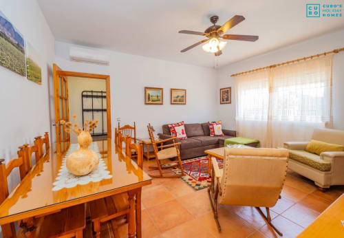 Amplio salón con mesa de comedor de madera, sofá marrón, butacas, ventilador de techo y abundante luz natural en el Riad