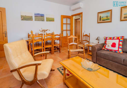 Sala de estar luminosa con muebles de madera, sillón crema, sofá gris, mesa de comedor y decoración colorida en Alhaurín de la Torre