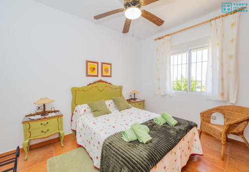Dormitorio luminoso con cabecero amarillo, almohadas verdes y ventilador de techo de madera en la villa Riad de Maruchi en Alhaurín