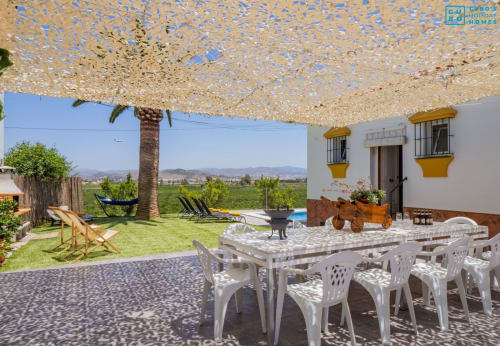Terraza exterior de la villa Riad de Maruchi con mesa de comedor, área de descanso sombreada y vistas a la montaña en Alhaurín de la Torre.