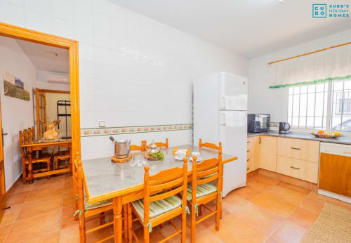 Luminosa cocina-comedor con mesa de madera naranja, sillas y mobiliario en villa de Alhaurín equipada con electrodomésticos modernos