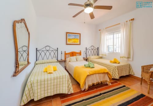 Dormitorio luminoso en Alhaurín Loft con tres camas, detalles amarillos, ventilador de techo y alfombra rayada