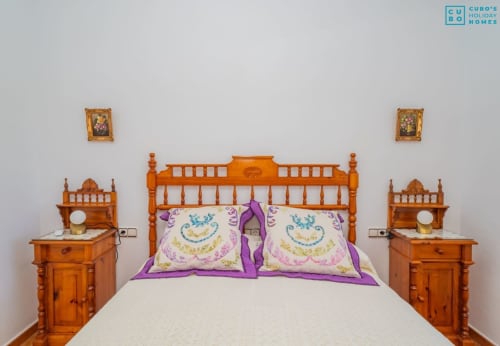 Habitación del Alhaurín Loft con cama de madera, almohadas púrpuras, mesitas de noche y arte decorativo enmarcado