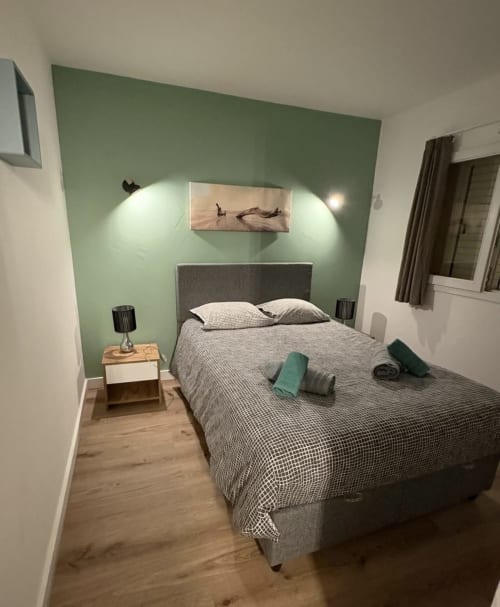 Chambre moderne à Tamaricciu Di Cala Rossa à Lecci avec mur d'accent vert sauge, lit gris et table de nuit en bois