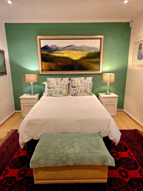 Luxury bedroom in Stellenbosch with green accent wall, mountain landscape painting, white bed with floral pillows, and red