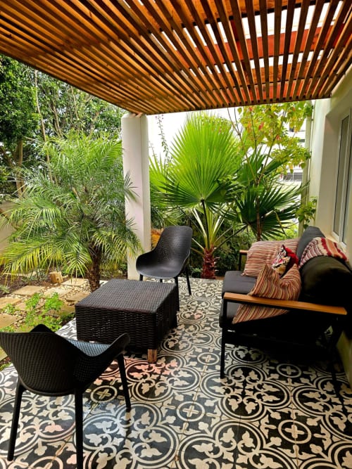 Shaded patio at Stellenbosch guest house with black modern seating, tropical plants, patterned tiles, and wooden pergola