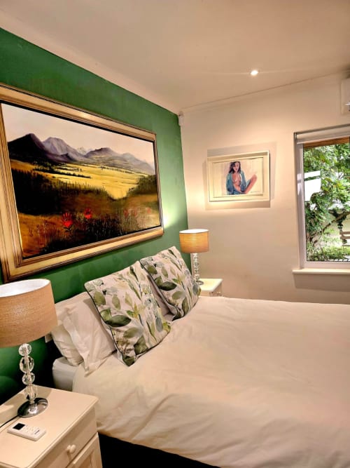 Stylish bedroom at Art House guesthouse in Stellenbosch with green accent wall, mountain landscape artwork, and garden view