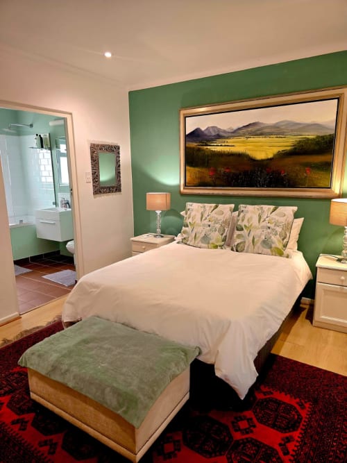 Stellenbosch guest bedroom with green accent wall, mountain landscape art, white bedding, and en-suite bathroom