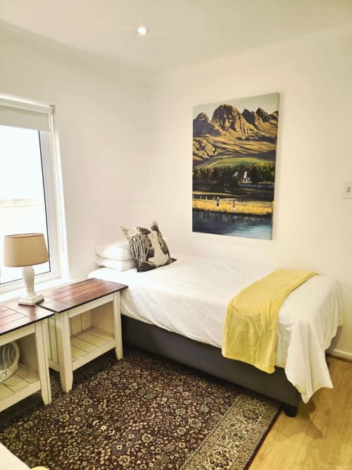 Bright bedroom at Guest Houses Italia in Stellenbosch with mountain view artwork, desk, lamp, and yellow accents