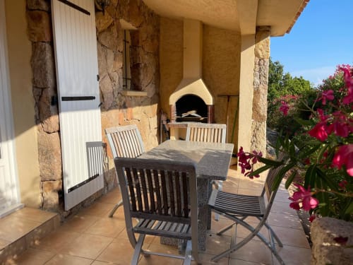 Terrasse ensoleillée de Vista D'oro avec table de dining, chaises, murs en pierre, bougainvillées en fleurs et four à pizza
