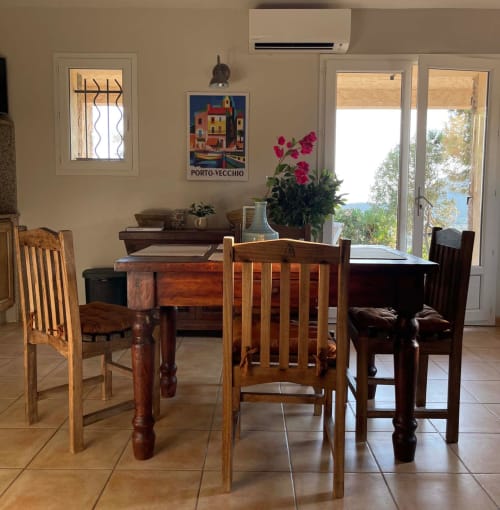 Salle à manger de Vista D'oro avec table en bois, chaises, fleurs magenta et vue sur mer par les portes-fenêtres à Monacia d'Aullène