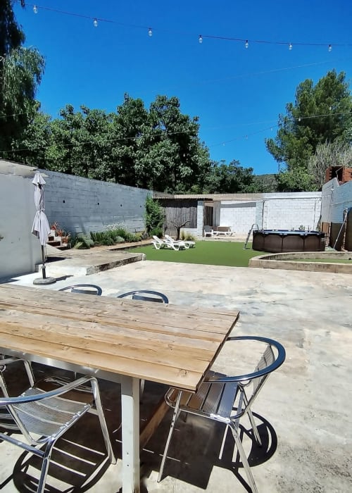 Amplio jardín trasero de la casa rural La Caseta de Ròtova con mesa de comedor de madera, tumbonas, piscina y vistas a las montañas