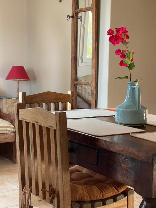 Élégante salle à manger à Vista D'oro : chaise en bois, table foncée, fleurs roses en vase bleu et miroir surplombant la vue mer