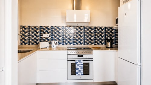 Cocina moderna en apartamento La Aldea con gabinetes blancos, azulejos geométricos azules, horno de acero inoxidable y madera
